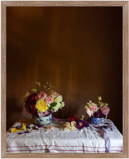 Framed still life arrangement with floral bouquets on a tablecloth against a dark background