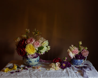 Still life floral with roses in blue and white jugs, on a white table cloth.