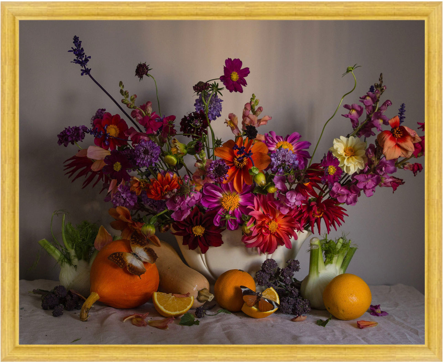 Framed still life arrangement with flowers, fruits, and vegetables on a tablecloth.