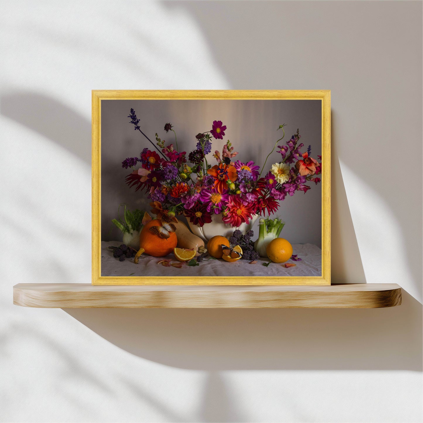 Framed still life with flowers and fruits on a wooden shelf against a neutral wall.