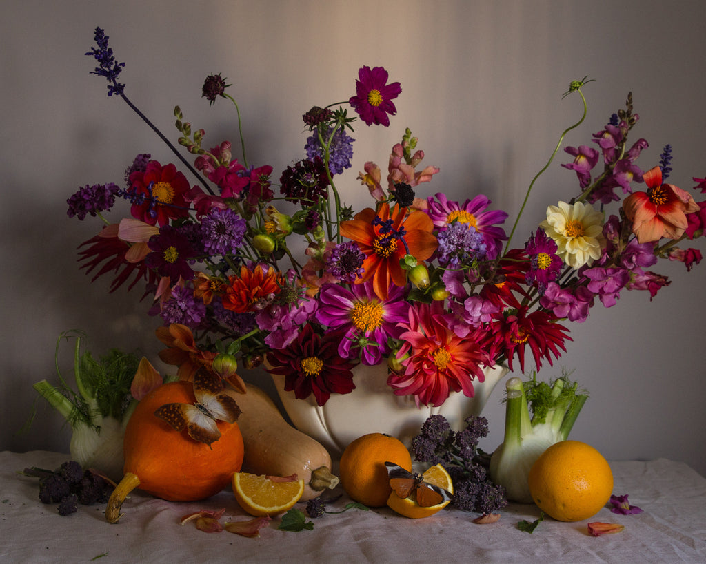 Fine art photograph by Emma Harris showing colorful floral arrangement in a white vase with pumpkins and oranges on a neutral background
