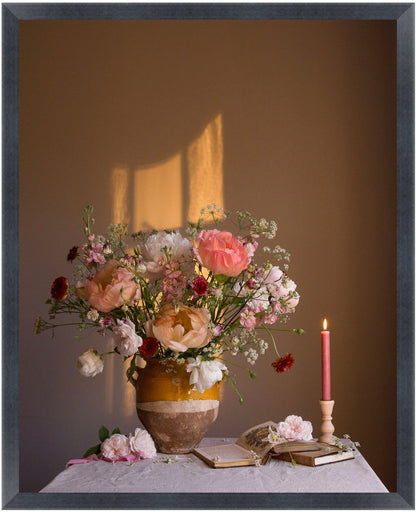 Floral arrangement in a vase with a candle and books on a table against a brown wall.   Flower still-life