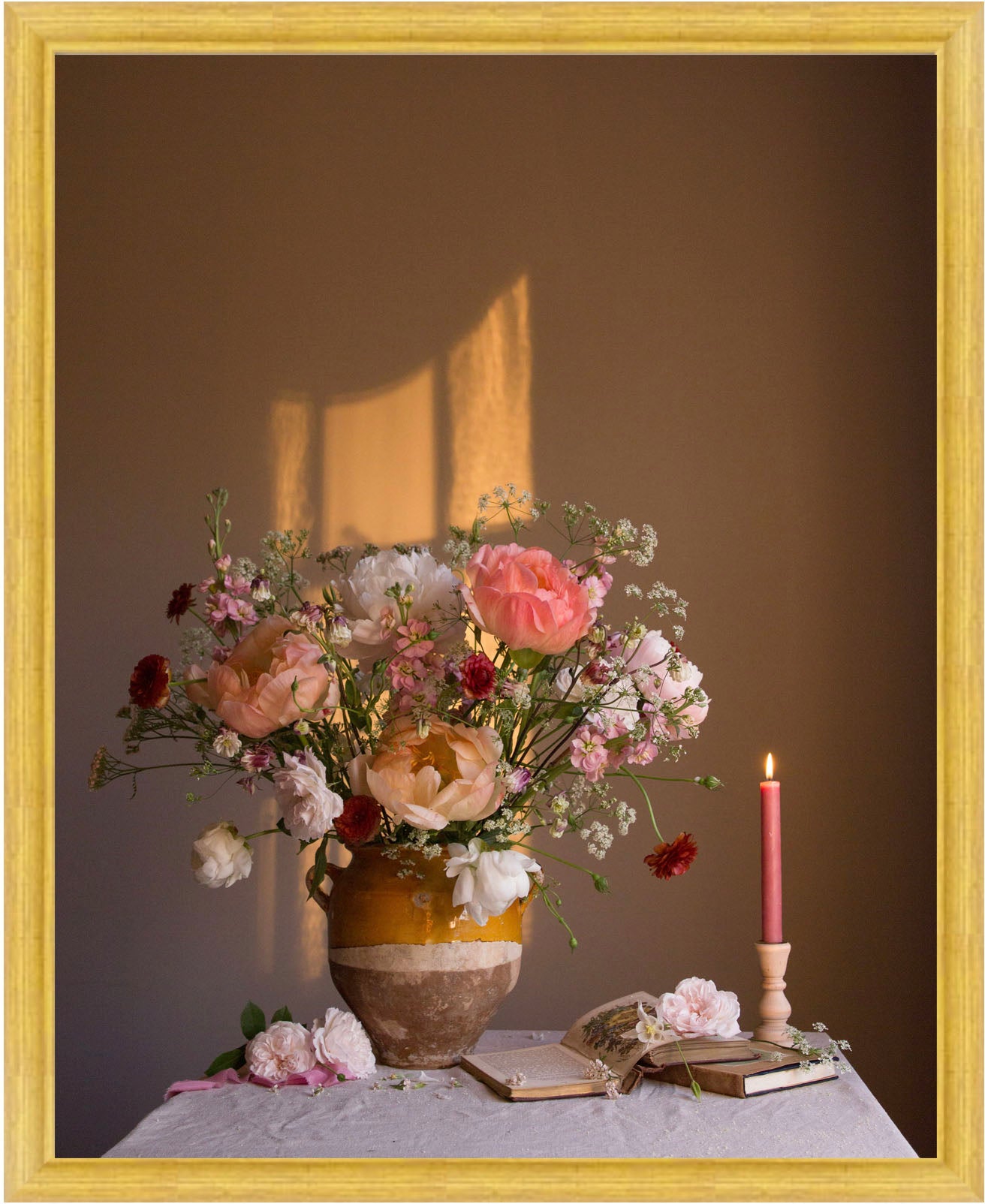 Floral arrangement in a vase with a candle and books on a table against a brown background.   Botanical still life