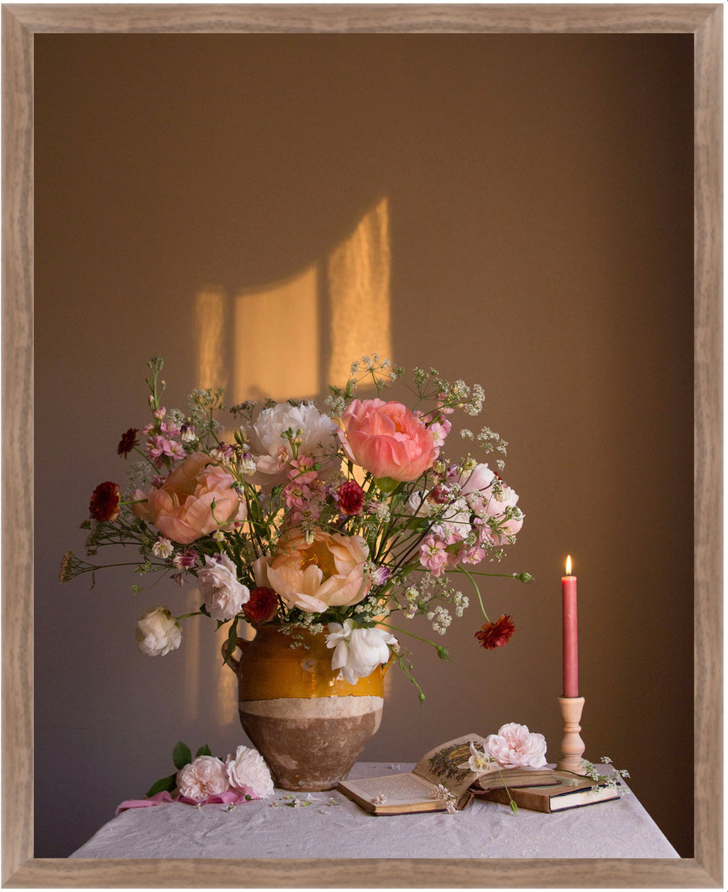Floral arrangement in a vase with candles and books on a table against a brown background.   Botanical print.