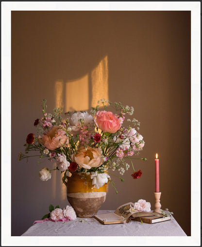 Floral Still-life with a candle and books on a table against a brown wall.