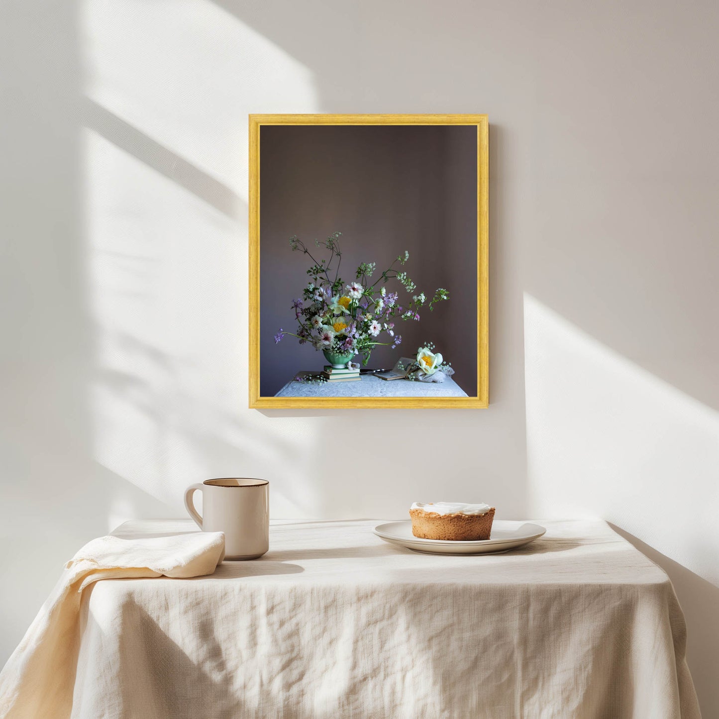Framed artwork of flowers on a wall above a table with a pie and cup.  Flower artwork