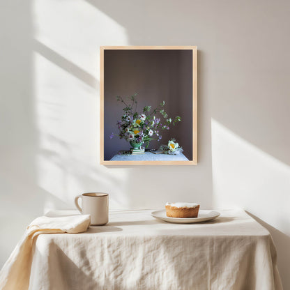 Framed artwork of a floral arrangement on a wall above a table with a pie and mug.   Floral artwork