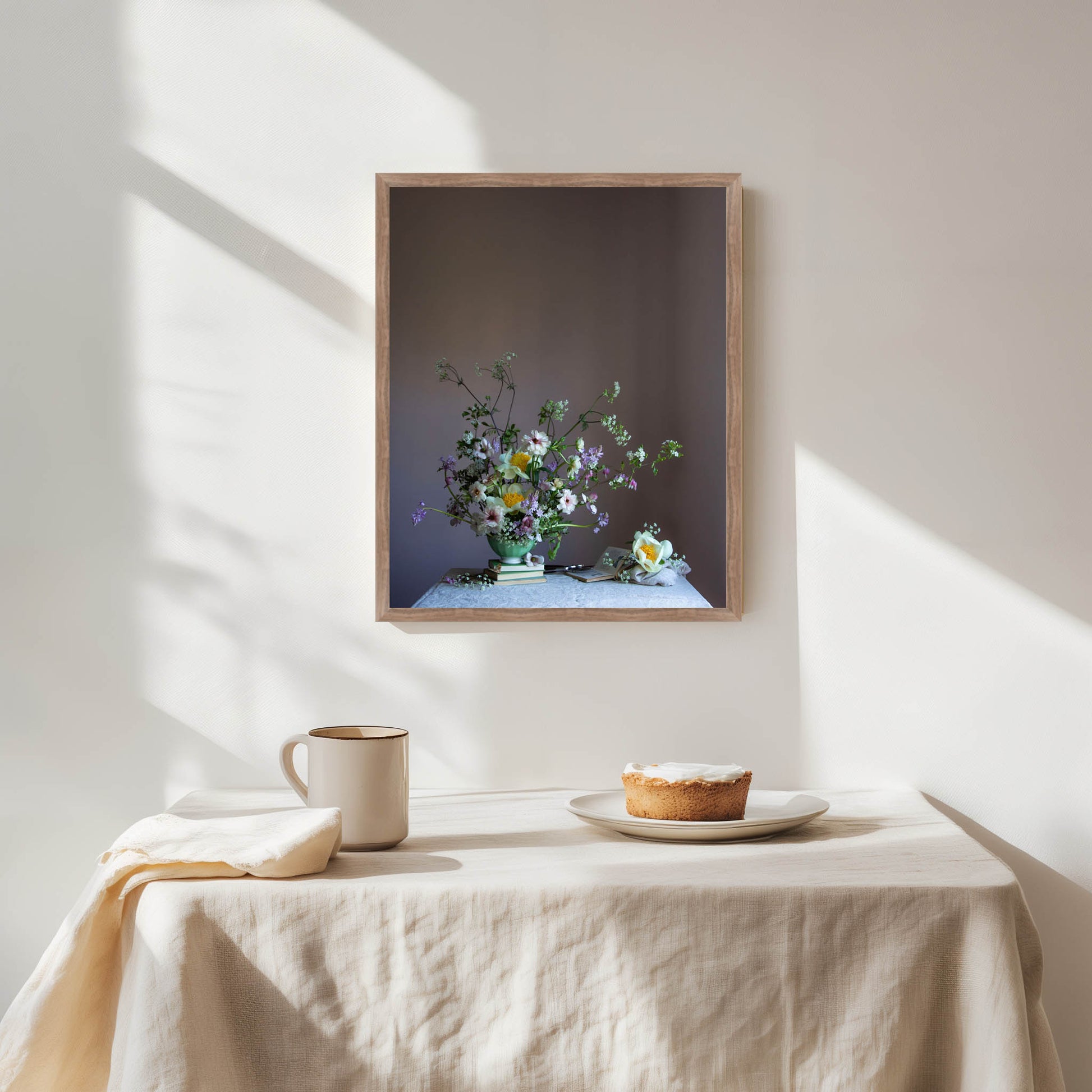 Framed artwork of a floral arrangement on a wall above a table with a pie and cup.   Botanical artwork