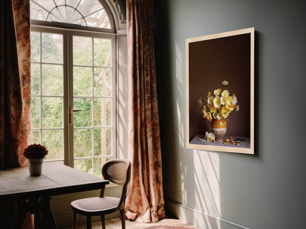 Room interior with a window, table, chair, and framed floral artwork on the wall.