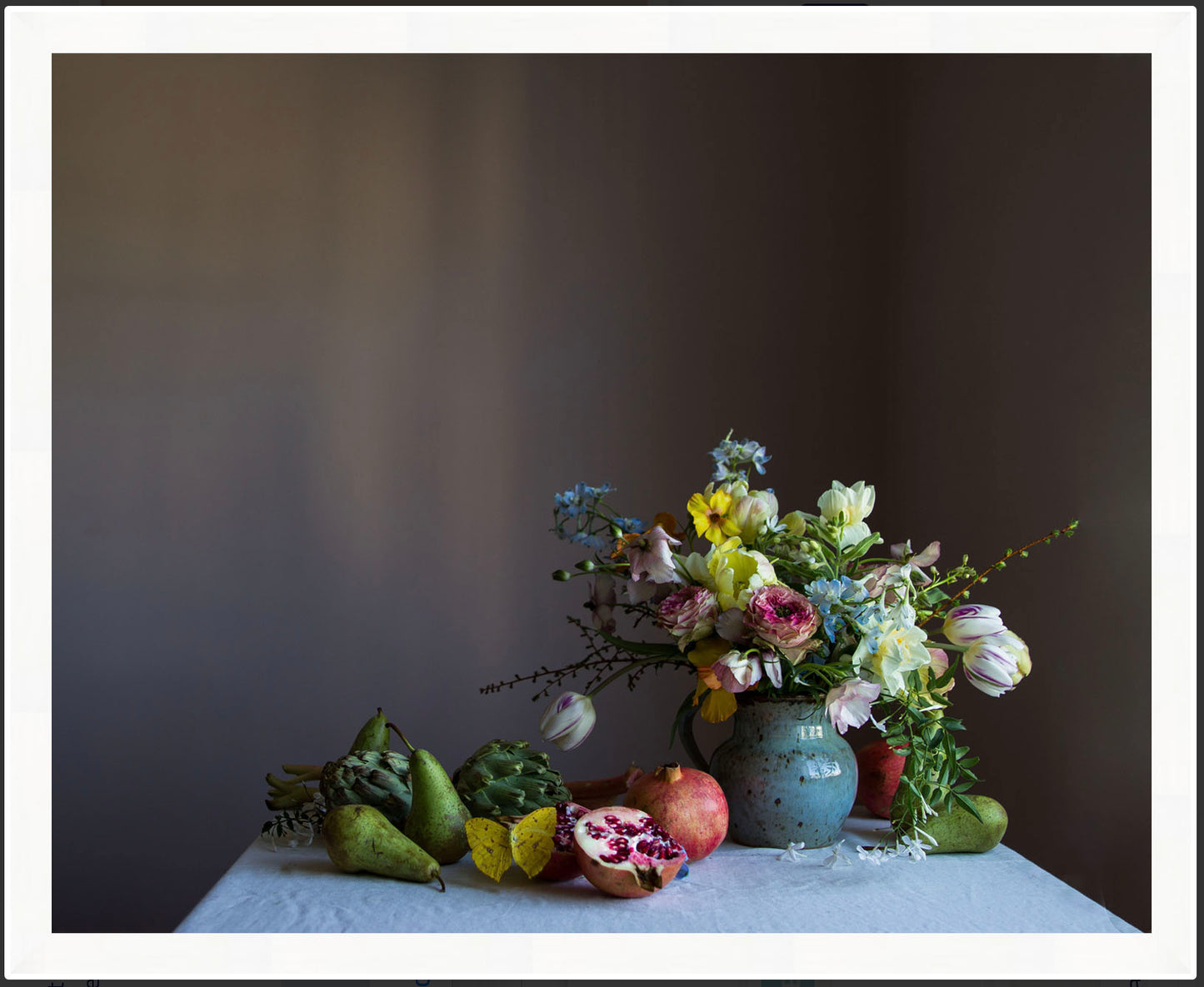 Vase of flowers with pears and a pomegranate on a table against a dark background. Floral art