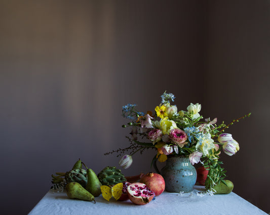 Still life with flowers, pears, and a pomegranate on a table against a dark background by photographer Emma Harris