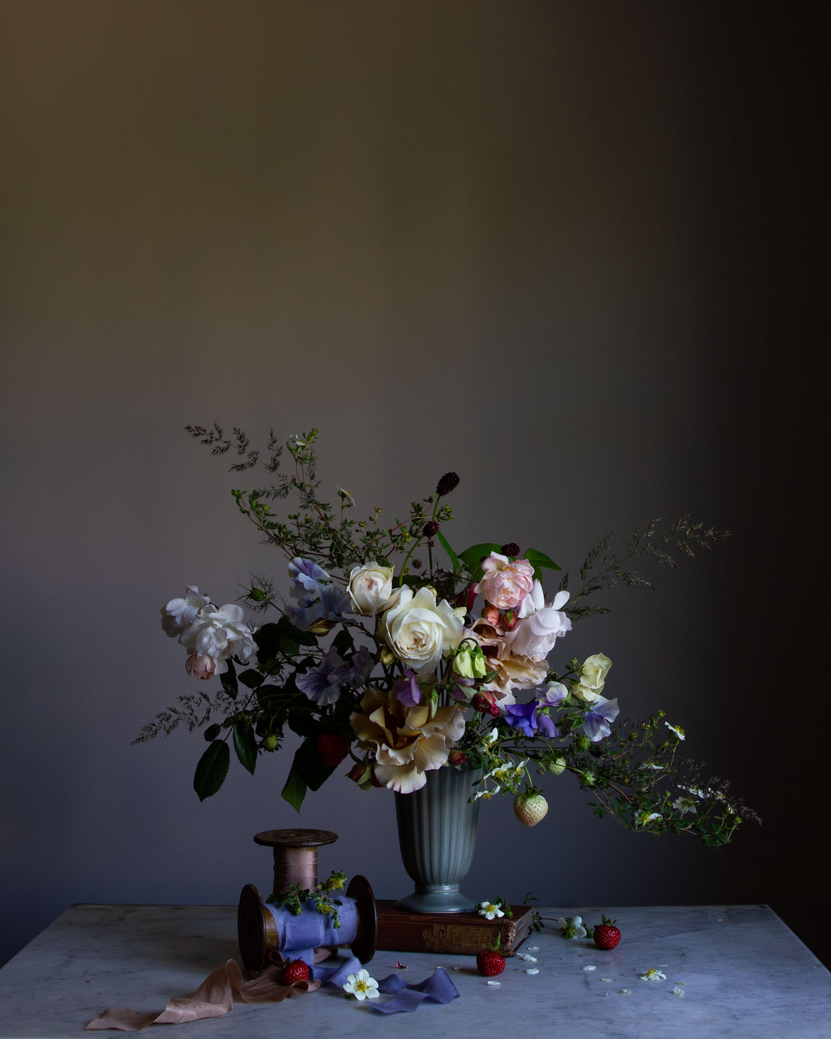 A fine art photograph featuring a floral arrangement with roses and other flowers in a vase, set against a dark background by photographer Emma Harris.   Floral art