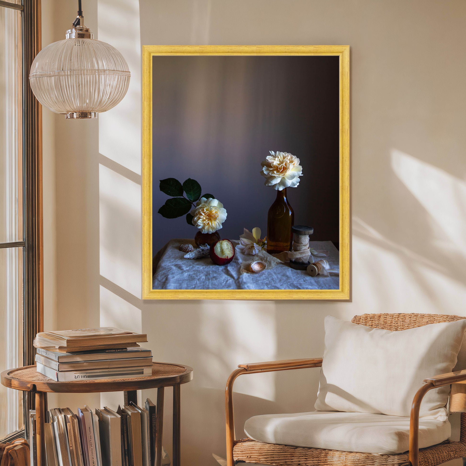 Framed artwork of flowers on a table in a room with a chair and books.   Floral picture.