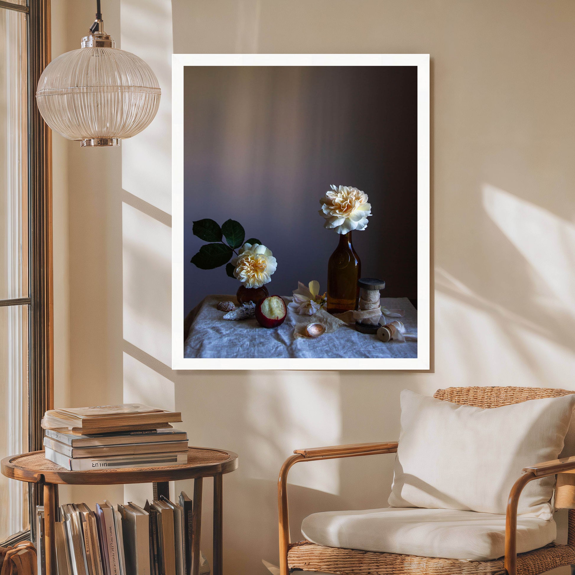 Framed artwork of flowers on a table in a room with a chair and books.   Still life picture