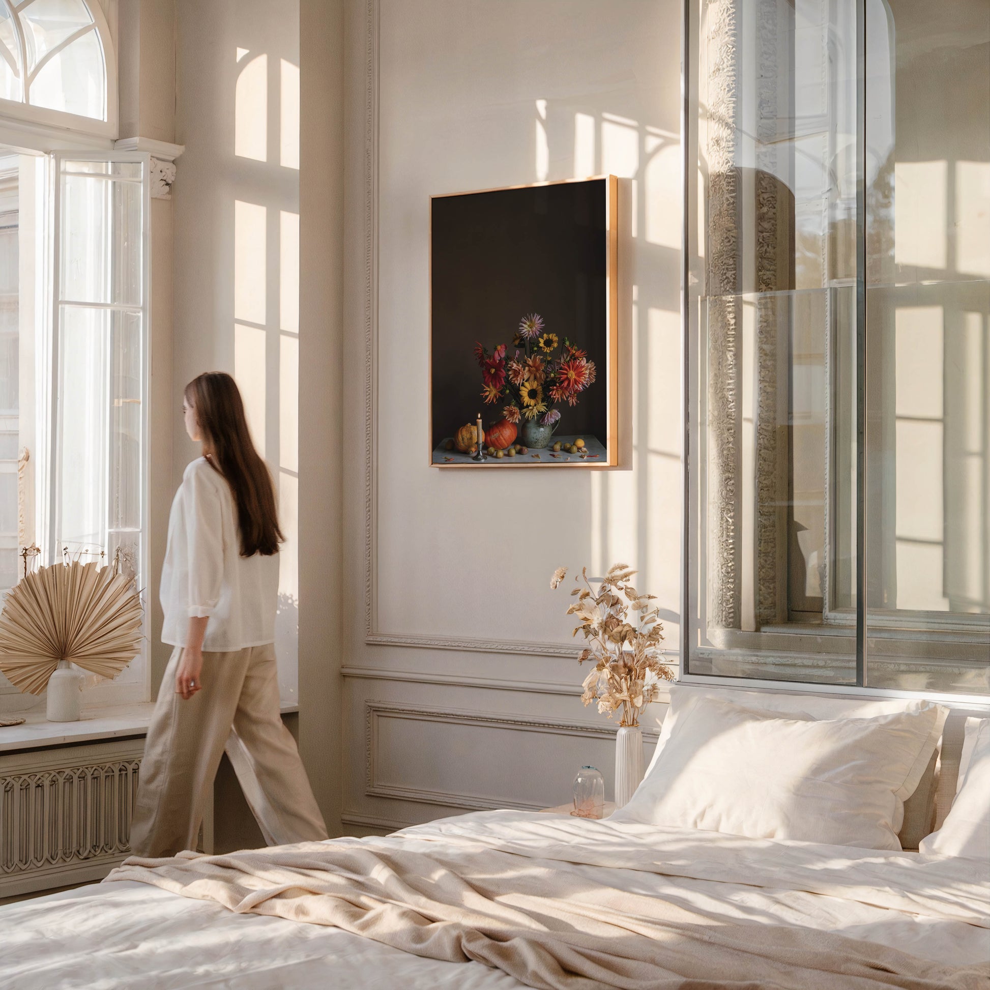 Woman in a bedroom looking at a picture of flowers on the wall.