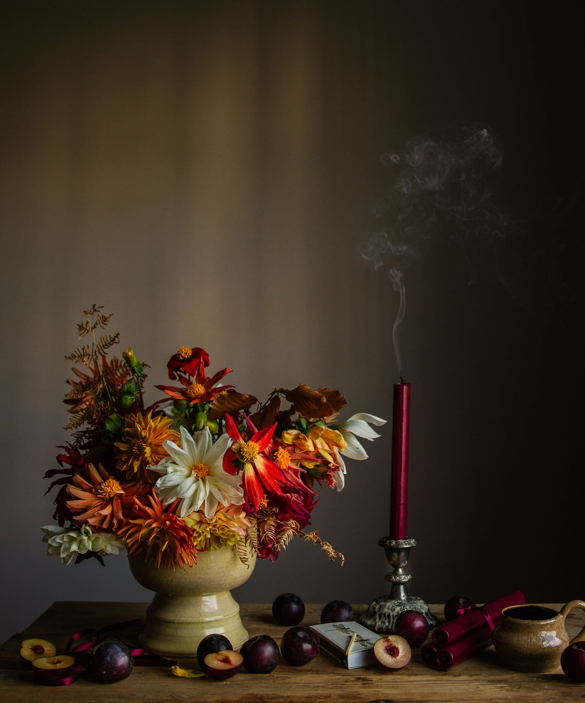 A limited edition fine art photographic print depicting a still life composition with a vibrant arrangement of flowers in an vase, alongside fruits and a smoking candle, set against a dark background by Emma Harris