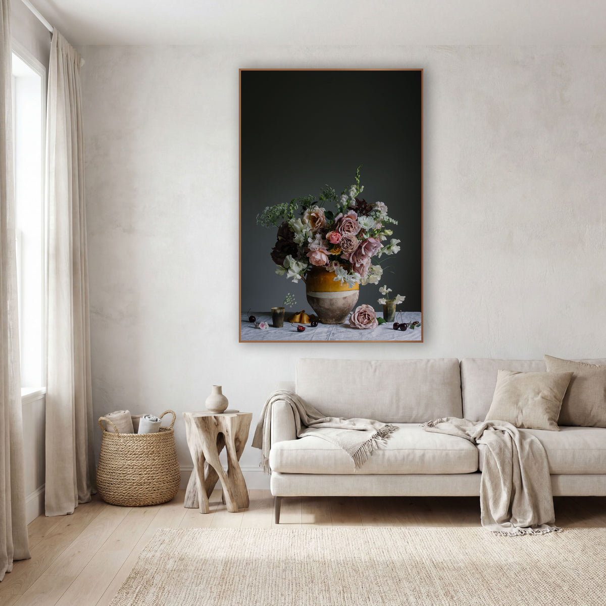 A framed vertical fine art print of a floral still life hanging on a textured off-white wall above a light beige sofa in a modern, minimalist living room.