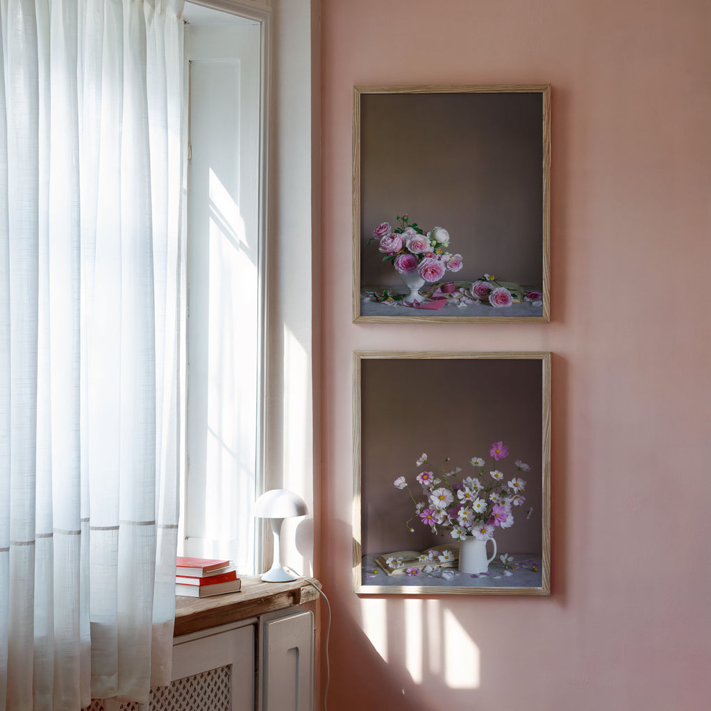 two still-life flower art prints framed in a pink room