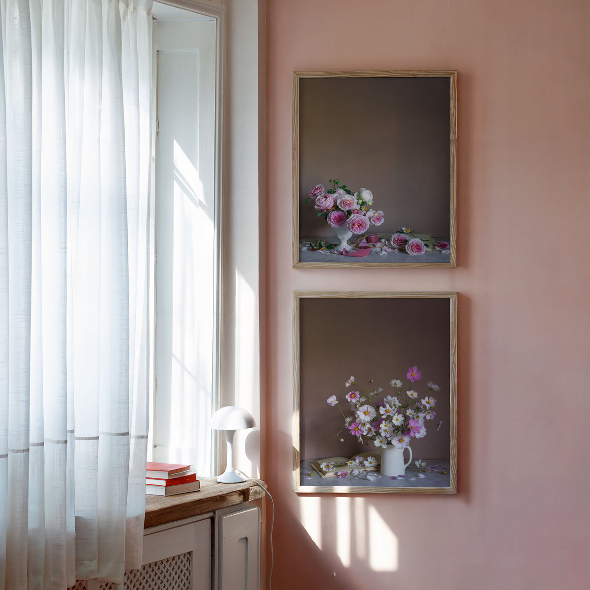 two still-life flower art prints framed in a pink room